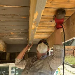 Handyman Services: photo shows a worker sanding the under side of a deck.